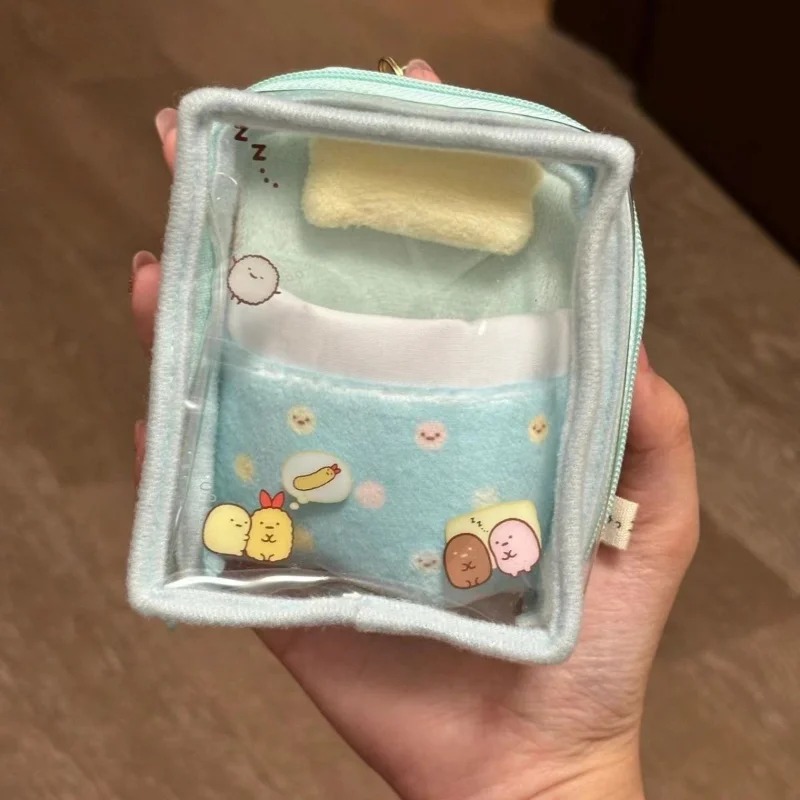 Mini bolsa transparente azul de Sumikko Gurashi em formato de caminha com travesseiro, segurada na mão