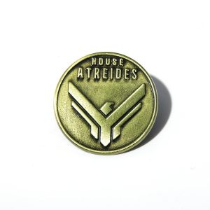 Broche redondo de metal bronze com o brasão da Casa Atreides, de Duna, em fundo branco