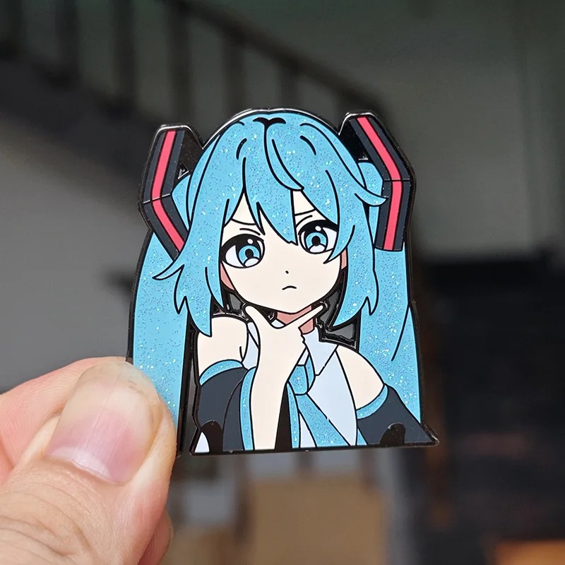 Broche esmaltado da Hatsune Miku preso entre os dedos para mostrar o tamanho