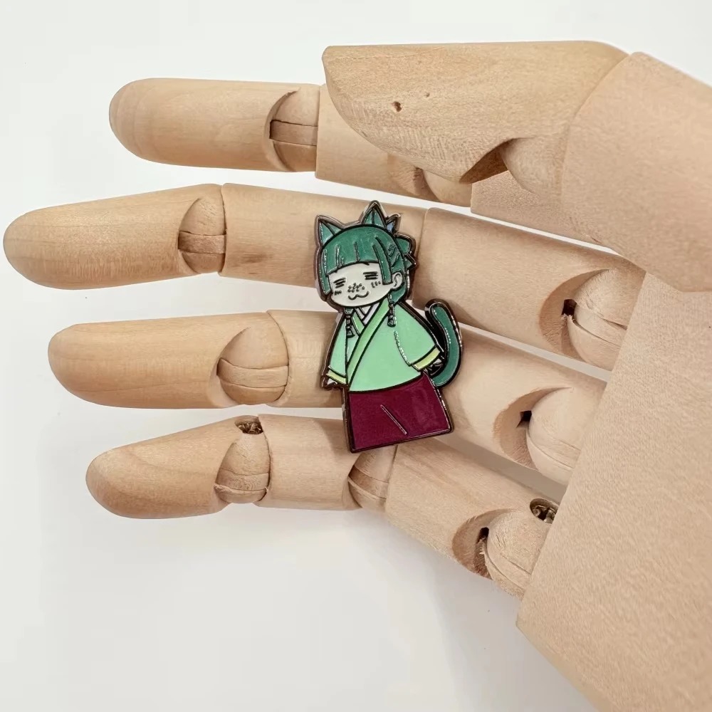Pin esmaltado da Maomao chibi apoiado na mão de um manequim de madeira para mostrar o tamanho