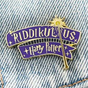 Pin esmaltado do feitiço Riddikulus, de Harry Potter, em faixa roxa com varinha dourada, sobre tecido jeans