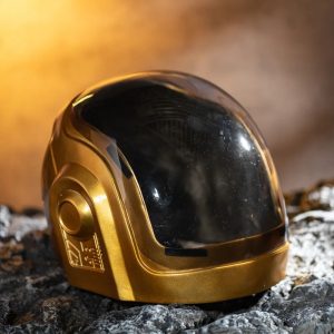 Capacete Daft Punk dourado de resina com viseira preta, estilo Guy-Manuel, sobre uma pedra