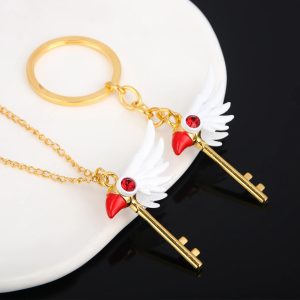 Chaveiro e colar de chave dourada com asas brancas e cristal vermelho de Cardcaptor Sakura sobre fundo preto e branco