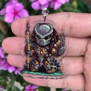 Chaveiro acrílico chibi do Predador, com máscara metálica e lança, segurado na palma da mão