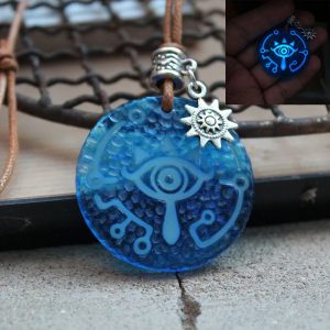 Chaveiro do Olho Sheikah de Zelda em verde-água sobre madeira, com argola e detalhe de sol prateado