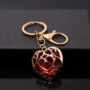 Chaveiro de Coração Container vermelho de Zelda em metal dourado, com argola e mosquetão, sobre superfície preta