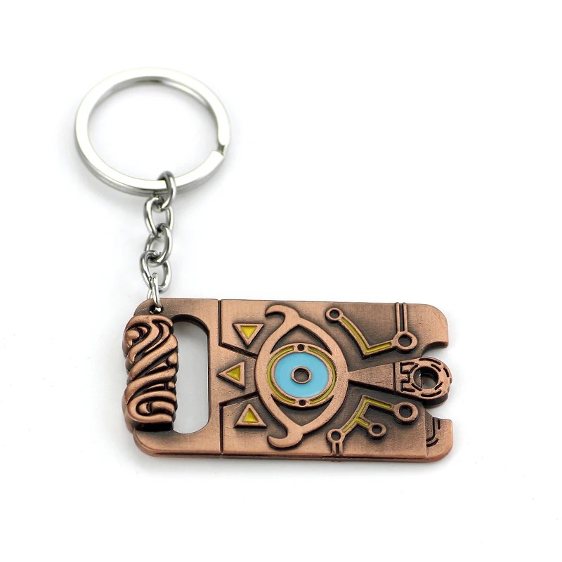 Chaveiro do Purah Pad de Zelda deitado, mostrando a placa com o Olho Sheikah e o detalhe superior