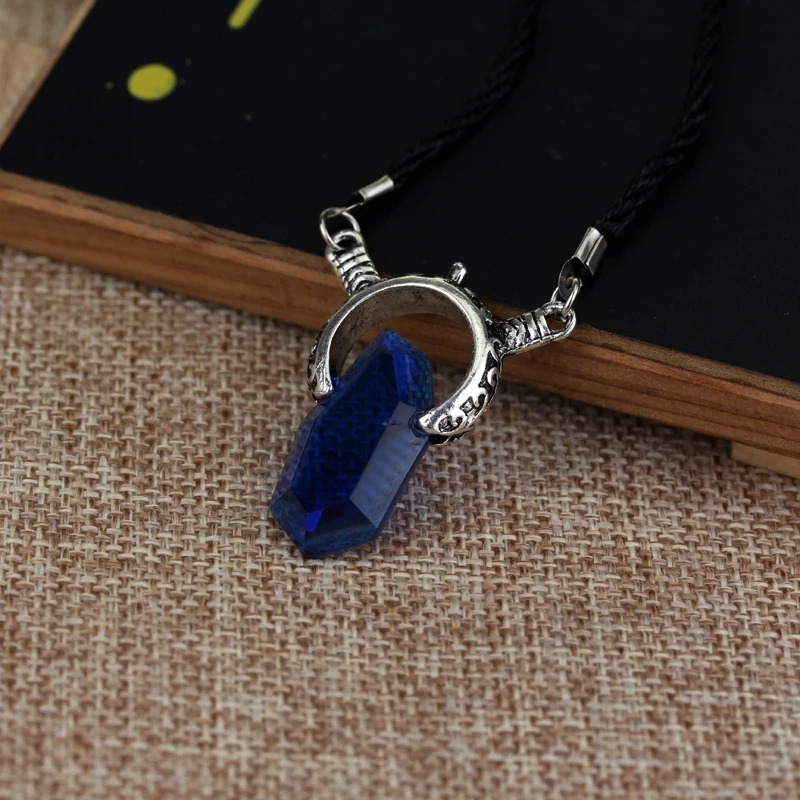 Colar de Dante com cristal azul escuro preso a argola metálica, sobre tecido de juta