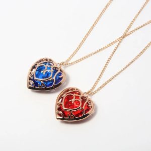 Dois colares de coração dourado de Zelda, um com pedra azul e outro com pedra vermelha, sobre fundo branco