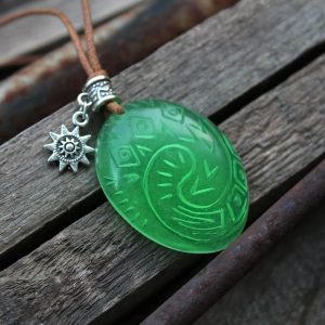 Pingente verde do Coração de Te Fiti, de Moana, com enfeite de sol sobre madeira