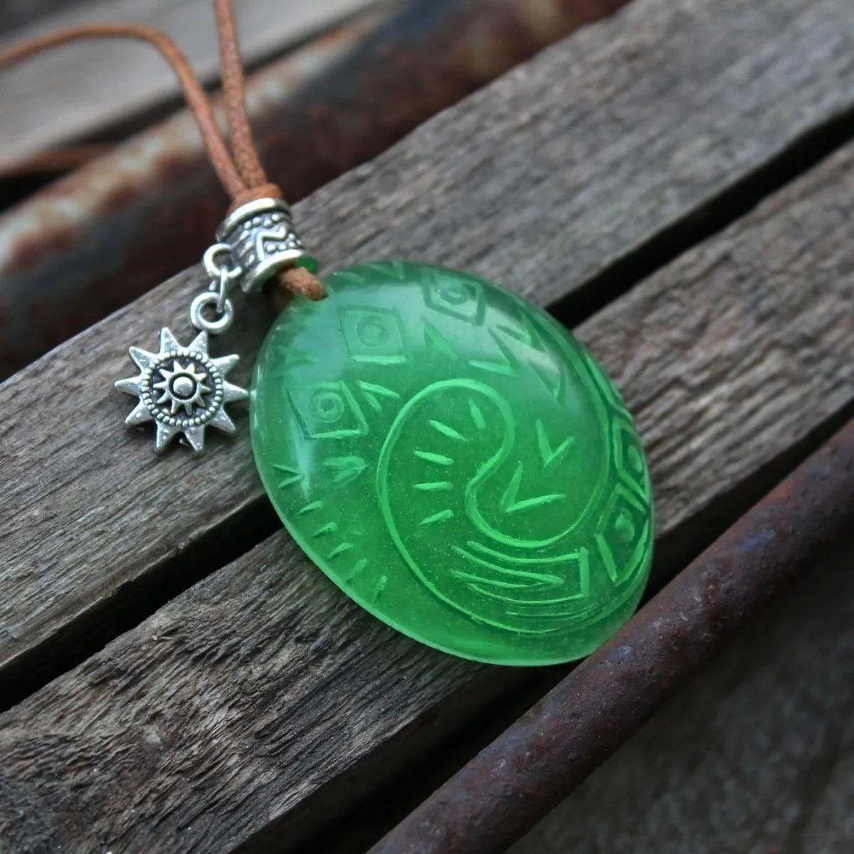 Pingente verde do Coração de Te Fiti, de Moana, com enfeite de sol sobre madeira