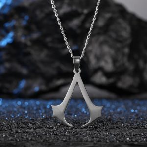 Colar prateado com pingente do símbolo de Assassin's Creed sobre fundo de pedras escuras