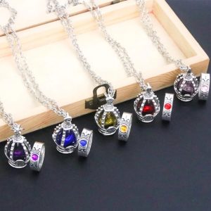 Cinco colares de soul gem de Madoka Magica com cristais de cores diferentes sobre uma caixa de madeira