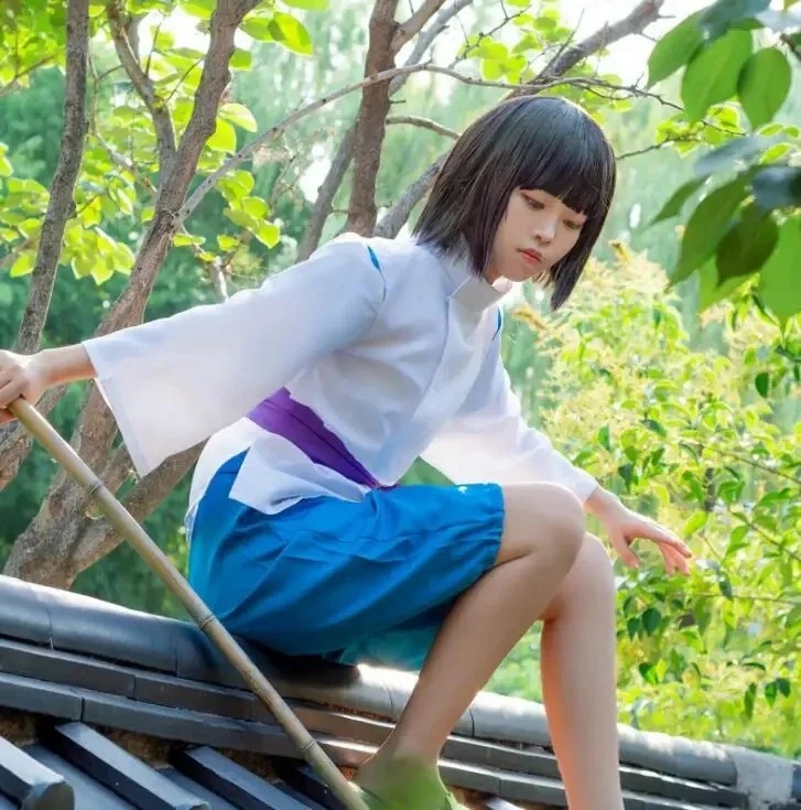 Cosplayer com o traje do Haku, de A Viagem de Chihiro, sentada em um telhado