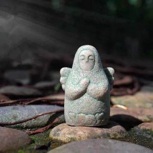 Estatueta da deusa de Breath of the Wild, com mãos em prece e asas, sobre pedras no jardim