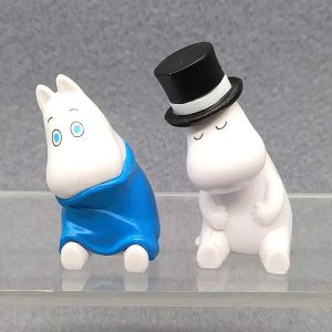 Figure branca do Moomin com capa azul ao lado do pai Moomin de cartola preta, em PVC