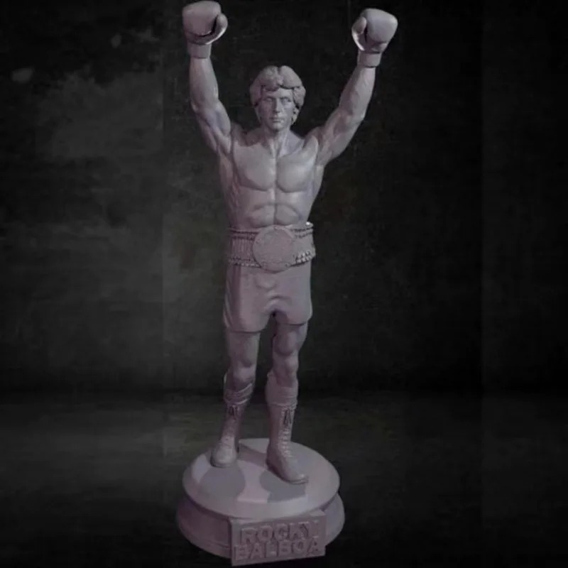 Miniatura em resina do Rocky Balboa de braços erguidos, com calção e cinturão, sobre fundo escuro