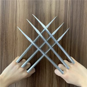 Par de garras prateadas de plástico no estilo do Wolverine cruzadas diante das mãos, sobre madeira