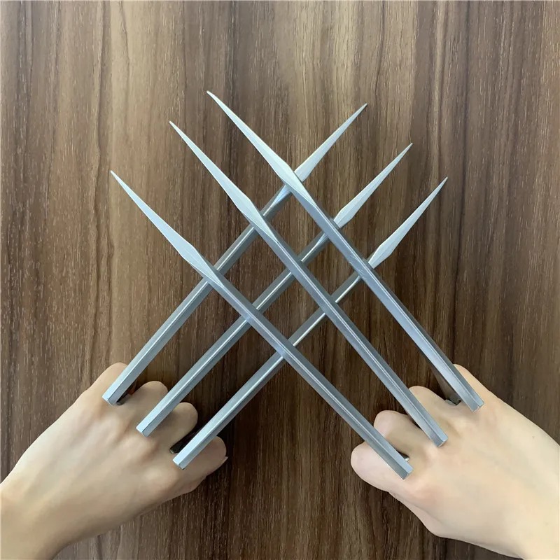 Par de garras prateadas de plástico no estilo do Wolverine cruzadas diante das mãos, sobre madeira