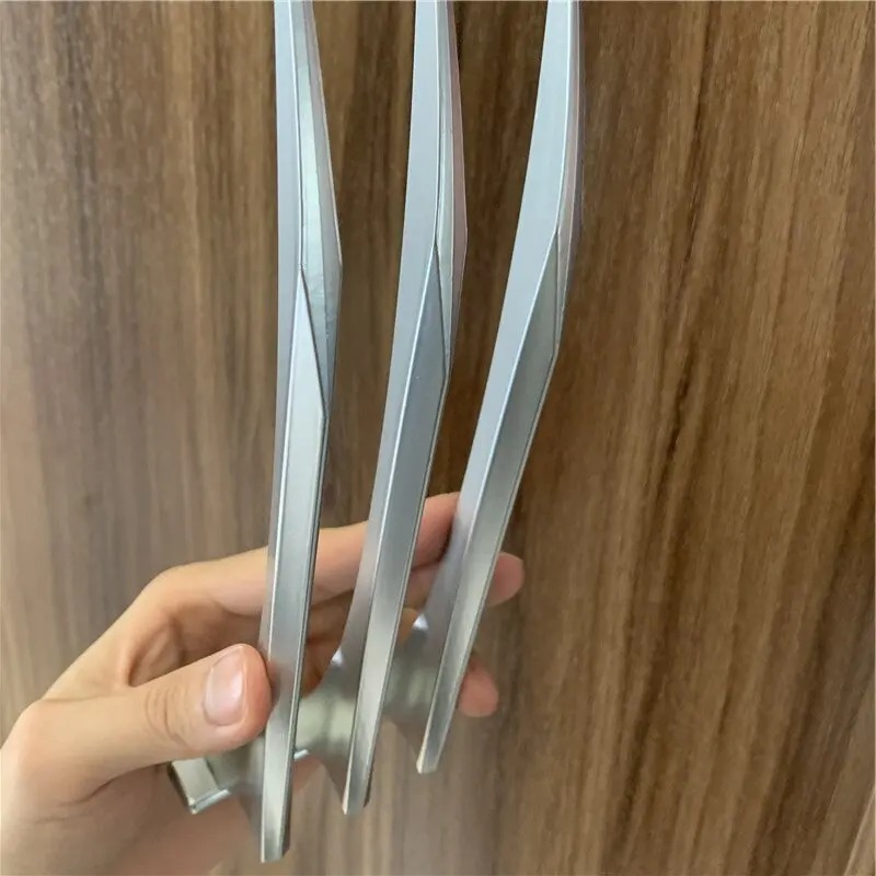 Detalhe das três garras prateadas presas a uma barra de dedos, segurada por uma mão