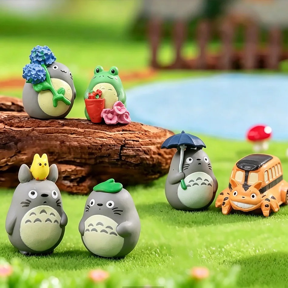Miniaturas do Totoro e do Gatobus em um jardim em miniatura, com sapo, guarda-chuva e flores