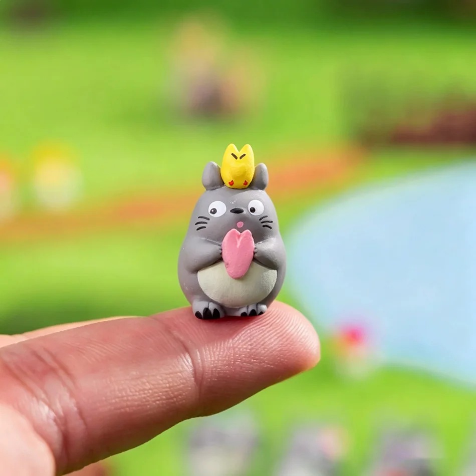 Miniatura do Totoro de 1,5 a 3 cm com um pássaro amarelo na cabeça, sobre a ponta de um dedo
