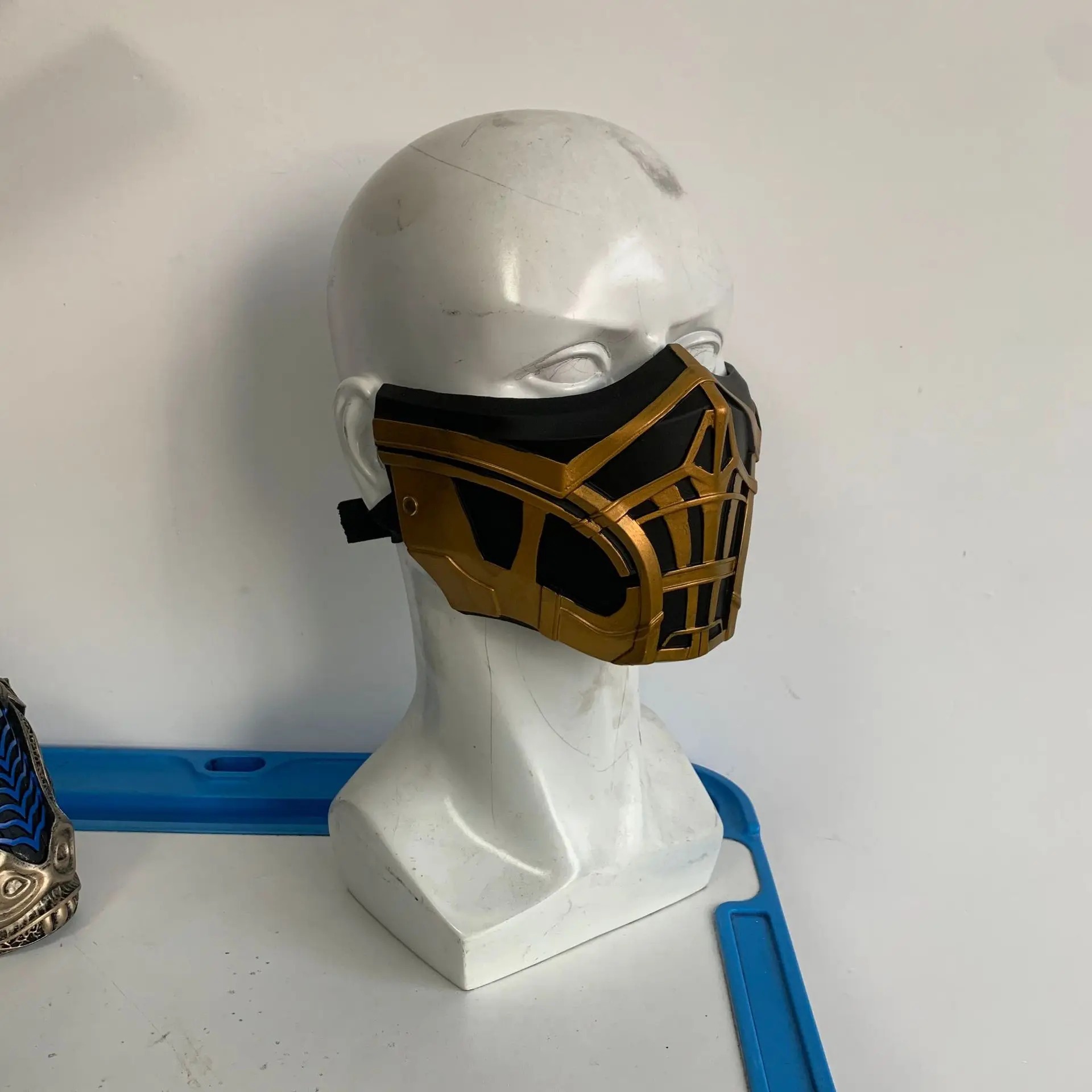 Máscara dourada e preta do Scorpion em um manequim, vista de frente