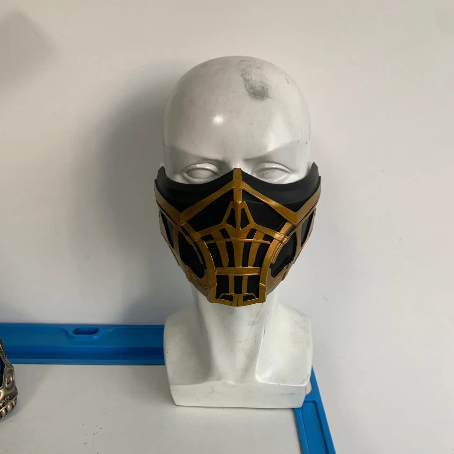 Máscara do Scorpion de Mortal Kombat em manequim, mostrando o acabamento dourado