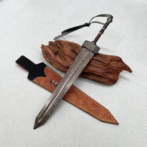 Miniatura da Greatsword de Elden Ring em metal, ao lado da bainha, apoiada em uma peça de madeira