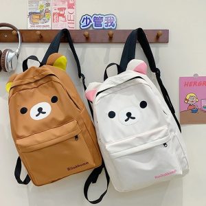 Duas mochilas do Rilakkuma, uma marrom e uma bege, com rosto do urso e orelhinhas penduradas em um cabideiro