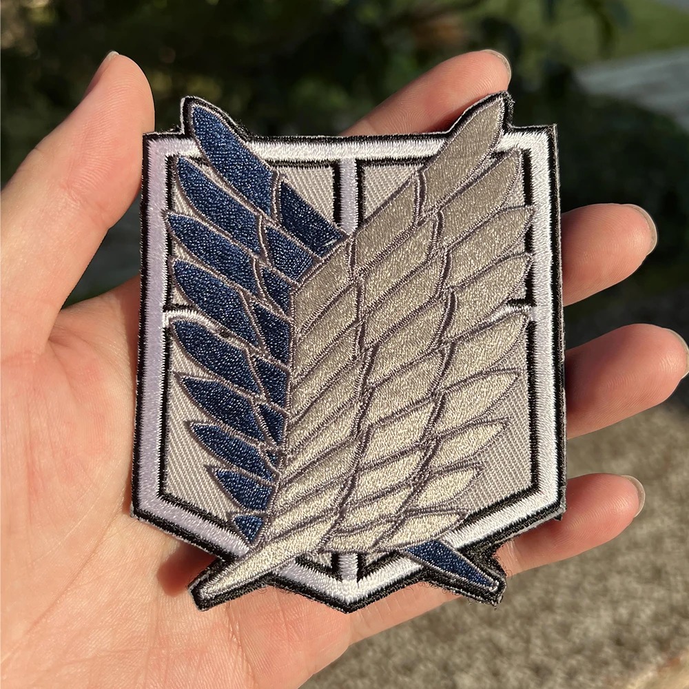 Patch das Asas da Liberdade, de Attack on Titan, segurado na mão para mostrar o tamanho