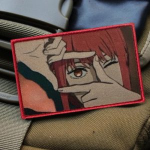 Patch da Makima, de Chainsaw Man, com os dedos enquadrando o olho e borda vermelha, sobre colete militar