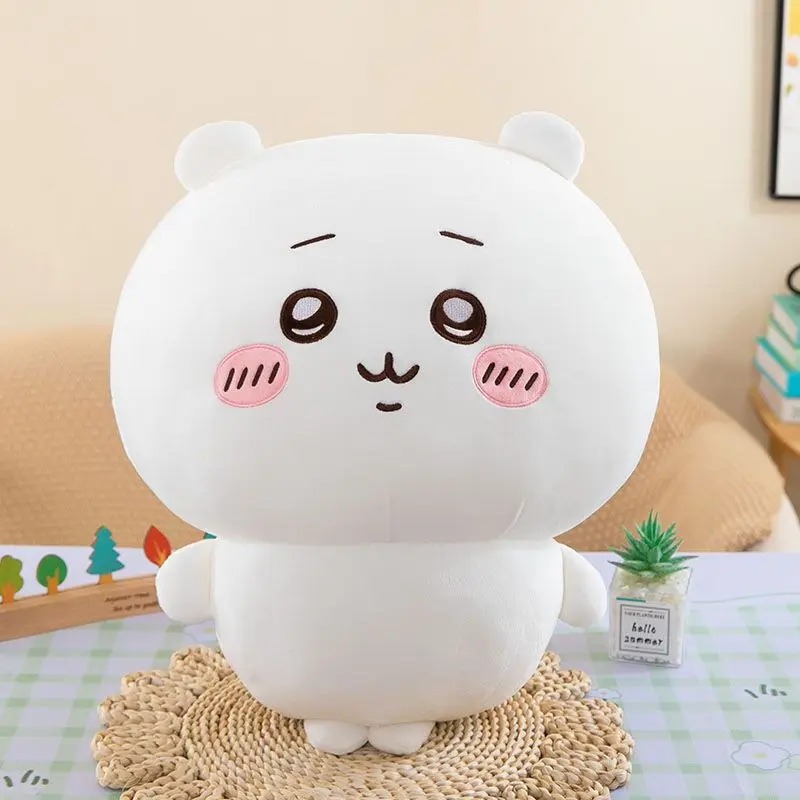 Pelúcia do Chiikawa, personagem branco e redondo com bochechas rosa, sentada sobre um apoio de palha
