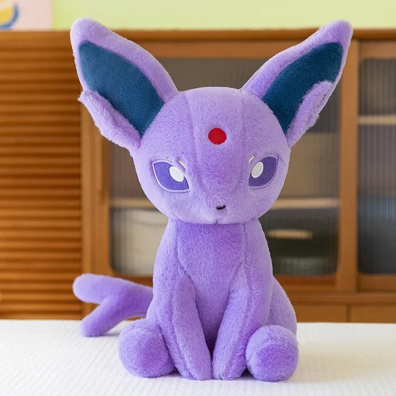 Pelúcia do Espeon, de Pokémon, lilás, sentada sobre uma mesa, em foto de produto