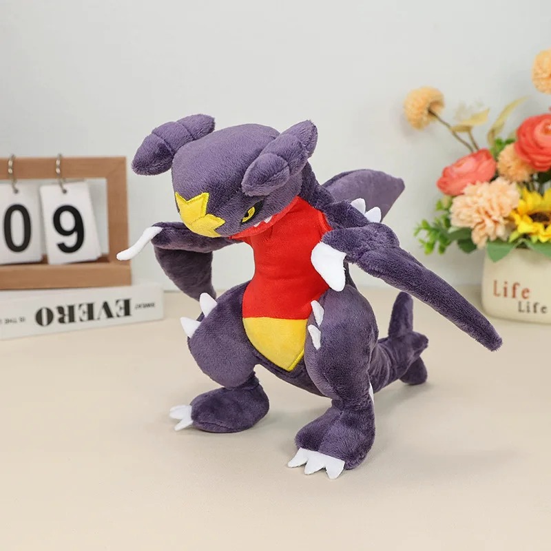 Pelúcia do Garchomp, de Pokémon, roxa com barriga vermelha e estrela amarela, sobre uma mesa