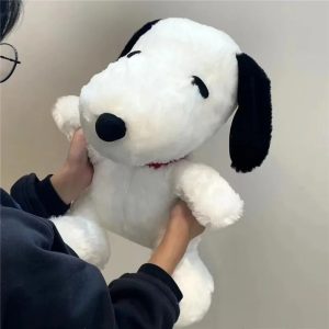 Pelúcia do Snoopy branca com orelhas pretas e coleira vermelha, segurada por uma pessoa