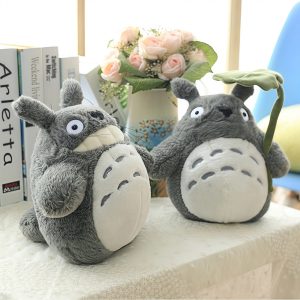Duas pelúcias do Totoro cinza com barriga clara sobre uma mesa, uma delas segurando uma folha de lótus