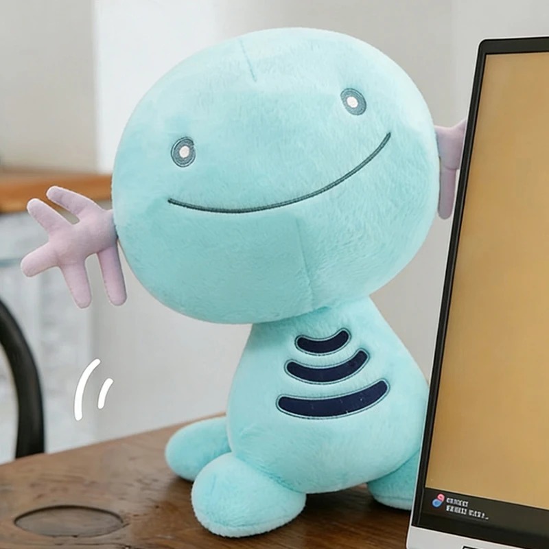Pelúcia do Wooper, de Pokémon, azul-turquesa, sentada sobre uma mesa, ao lado de um monitor