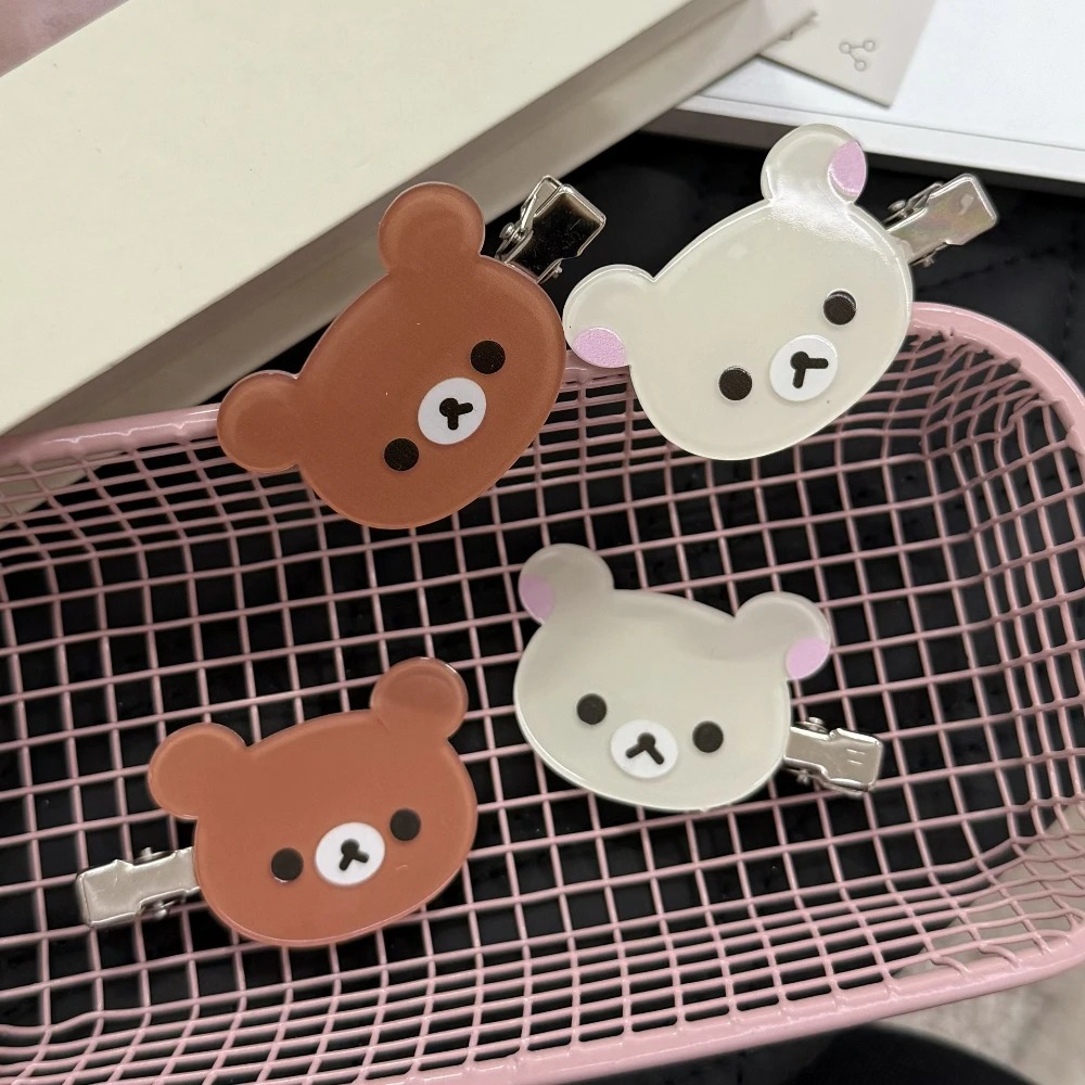 Quatro presilhas em formato de cabeça de urso do Rilakkuma em marrom e bege sobre cesto rosa