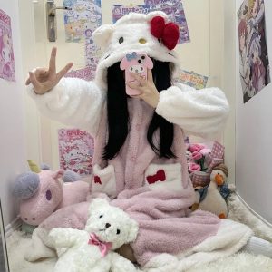 Pessoa com roupão rosa e branco da Hello Kitty com capuz de orelhinhas e laço vermelho, sentada em um quarto
