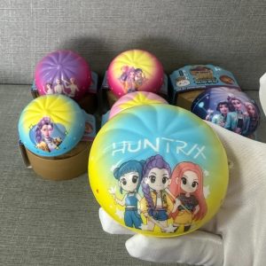 Mão com luva branca segurando um squishy amarelo e azul em forma de pãozinho com a estampa das HUNTR/X