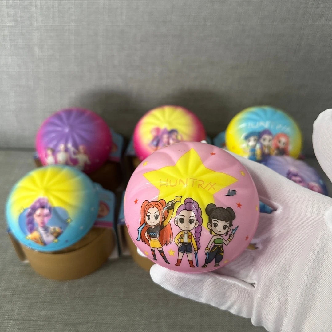 Squishy rosa com estrela amarela e desenho das três caçadoras HUNTR/X segurado por uma luva branca