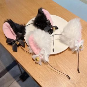 Três tiaras com orelhas de gato de pelúcia preta e branca, com laço e guizo dourado, sobre uma mesa